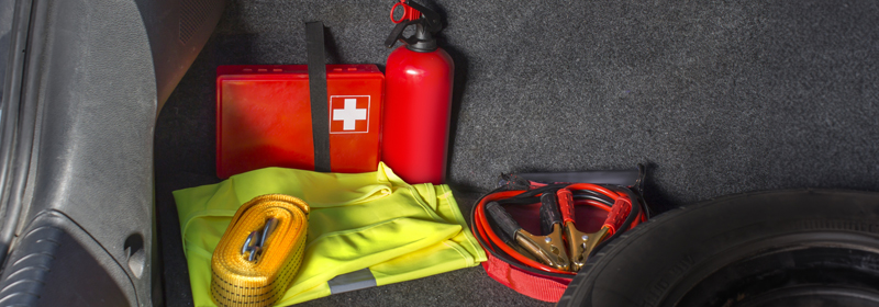 A picture of an emergency kit in a car, featuring a first-aid kit, a fire extinguisher, a tow strap, jumper cables, and a reflective vest.